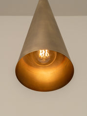 A cone-shaped pendant light fixture with a brushed brass exterior and a warm gold interior, illuminated with a visible Edison bulb.
