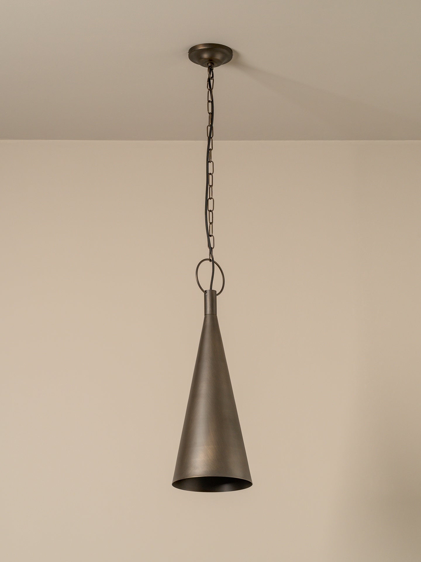 A single pendant light with a dark bronze metal cone shade hanging from a matching ceiling canopy and chain against a plain beige wall.