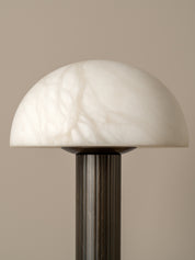 A mushroom-shaped table lamp with a white marble dome shade and a dark fluted metal stem, set against a solid beige background.