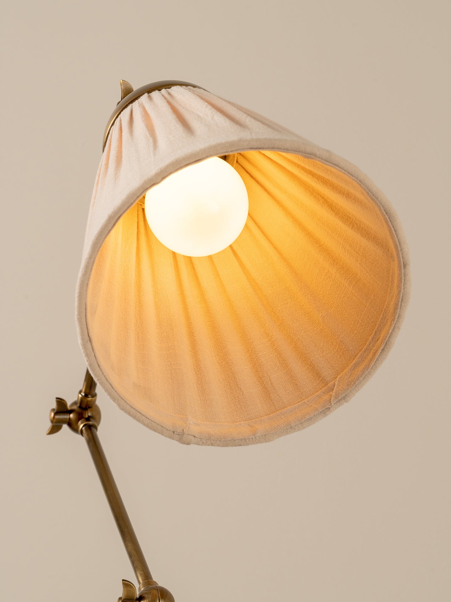 Wall-mounted lamp with a beige shade and brass arm on a neutral background