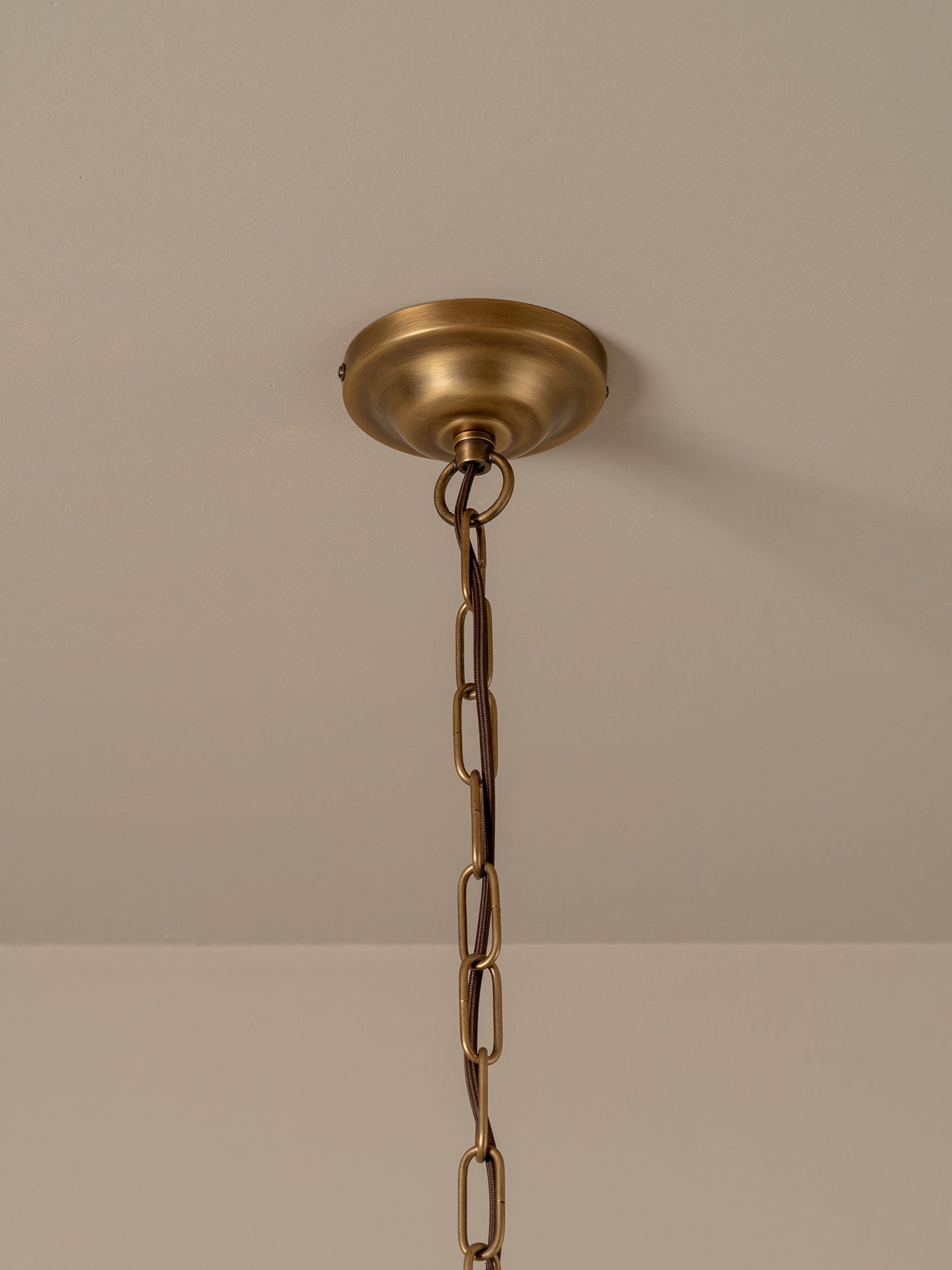 A brass ceiling light fixture canopy and hanging chain against a neutral beige wall and ceiling.