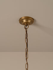 A brass ceiling light fixture canopy and hanging chain against a neutral beige wall and ceiling.