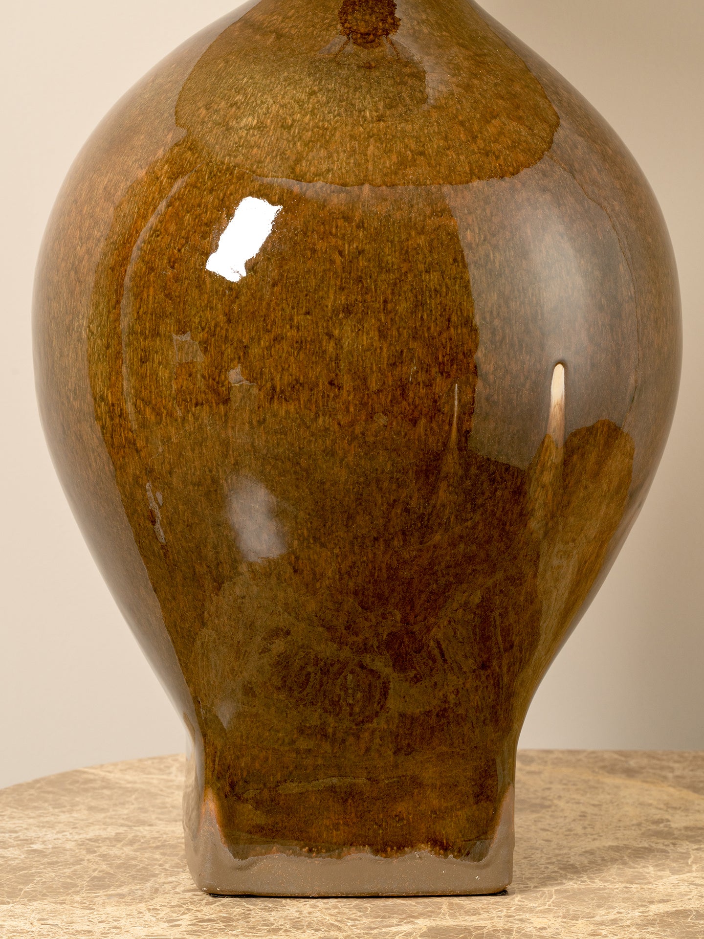 A glossy ceramic vase with a rounded bulbous body and a short flared base, shown on a stone-like surface against a plain light beige background.
