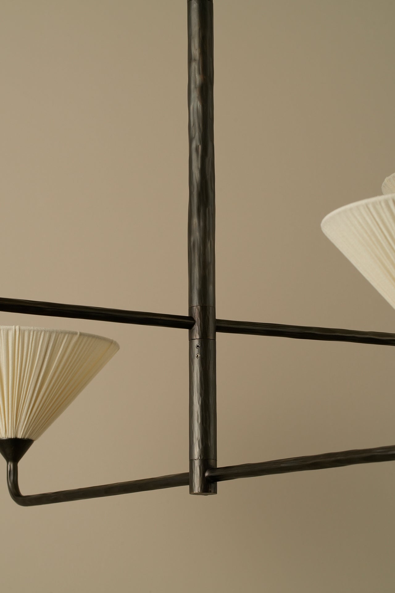 Close-up of a modern chandelier with a dark metal frame and pleated off-white fabric shades against a warm beige background.