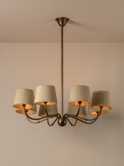A six-light chandelier with a dark bronze metal frame and beige fabric drum shades, shown hanging against a neutral beige wall and ceiling.