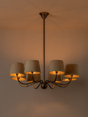A multi-light chandelier with a dark bronze metal frame and six tapered beige fabric shades, shown illuminated against a warm beige wall and ceiling.