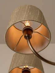 Close-up of a multi-light ceiling fixture with two drum shades in a textured beige fabric, featuring a warm orange-gold interior and a dark bronze metal frame with visible light bulbs.