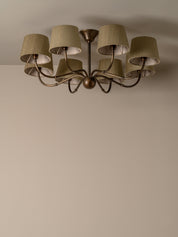 A six-light ceiling fixture with drum shades, shown mounted on a plain beige wall and ceiling.