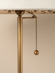Close-up of a brass pull chain lamp switch with a spherical ball finial hanging from a horizontal arm on a lamp post.