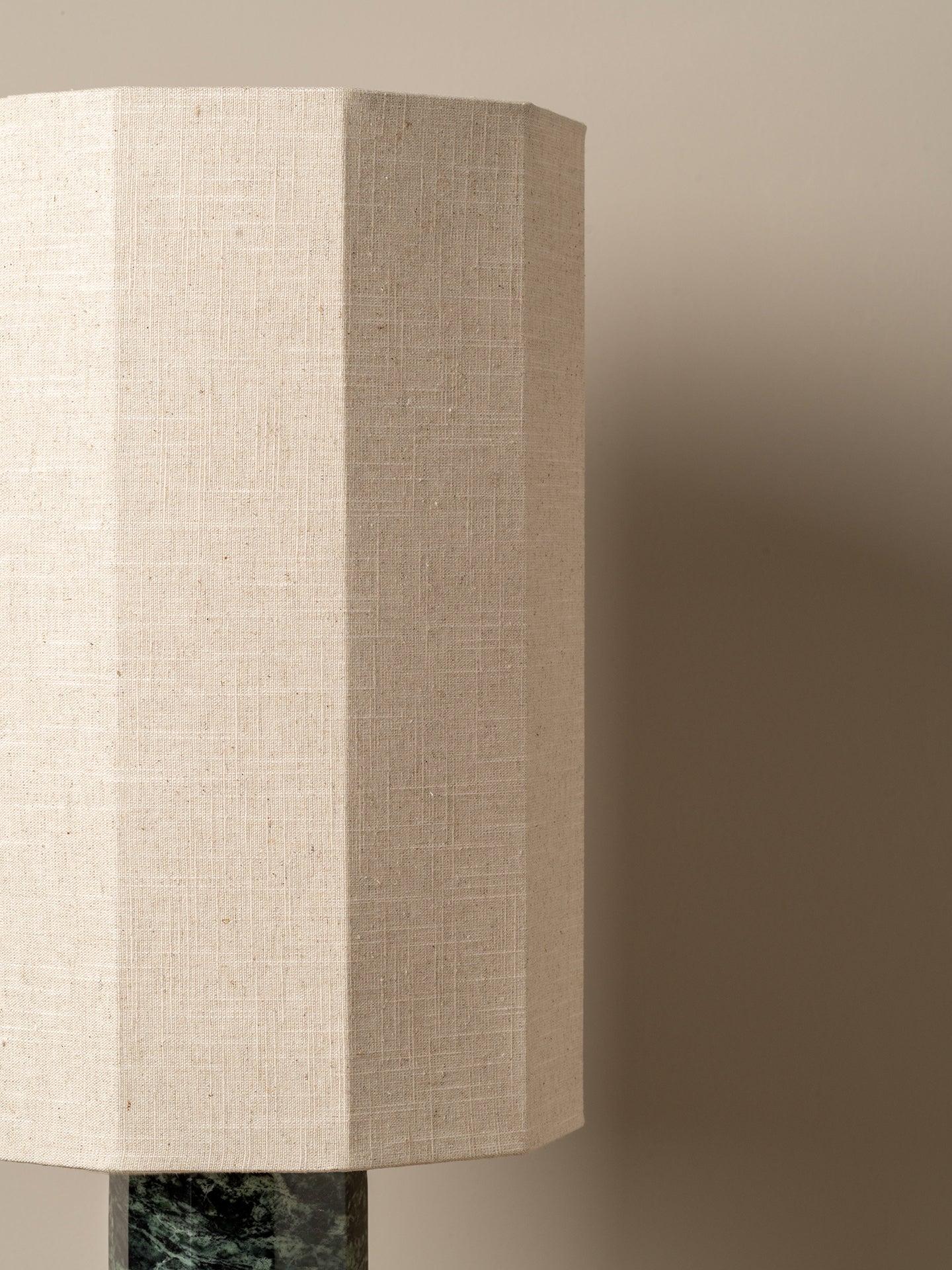 Close-up of a beige linen drum lampshade with a dark green marble base against a warm taupe background.