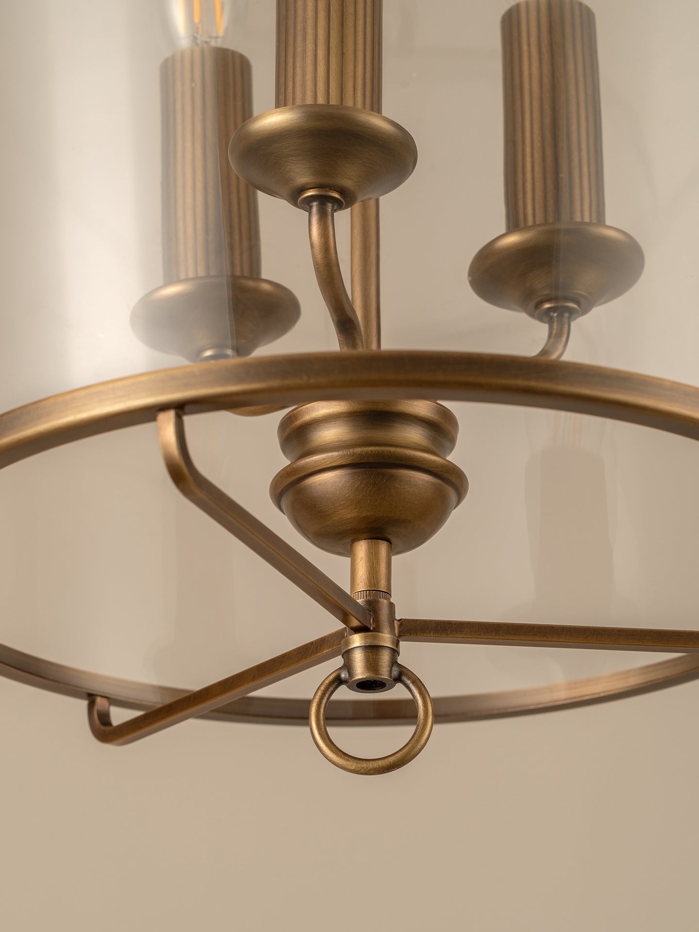 Close-up of an antique bronze chandelier light fixture showing the central stem, decorative ring, and two candle-style bulbs against a soft beige background.