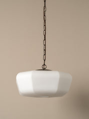 A modern pendant light with a wide, rounded white glass shade suspended from a black metal chain against a solid beige background.