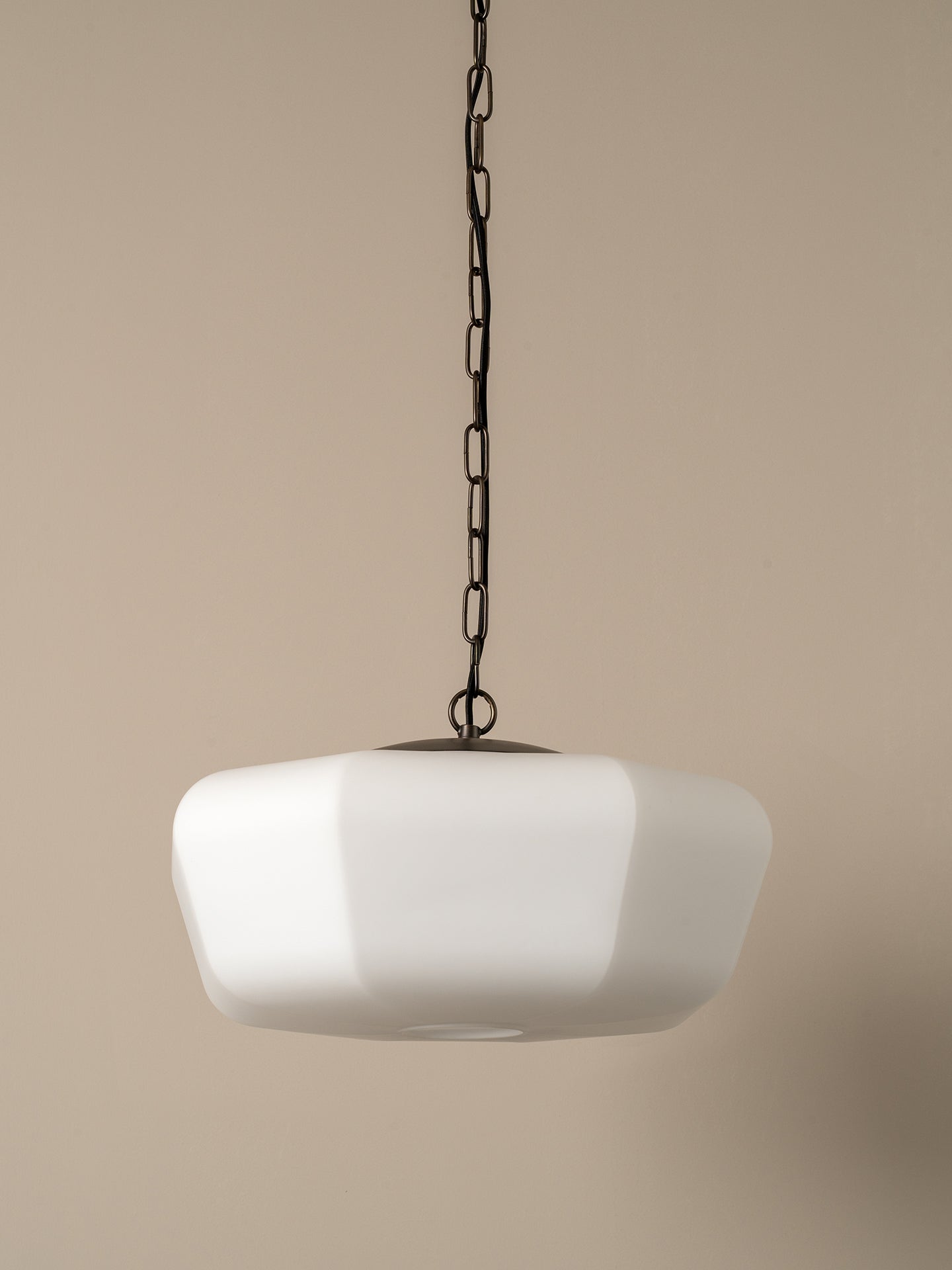 A modern pendant light with a wide, rounded white glass shade suspended from a dark metal chain against a solid beige background.