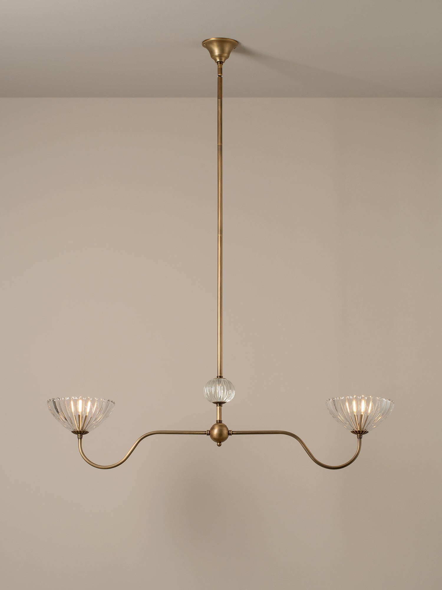 A three-light brass chandelier with a central glass globe and two curved arms ending in fluted clear glass shades, shown hanging against a plain beige wall.