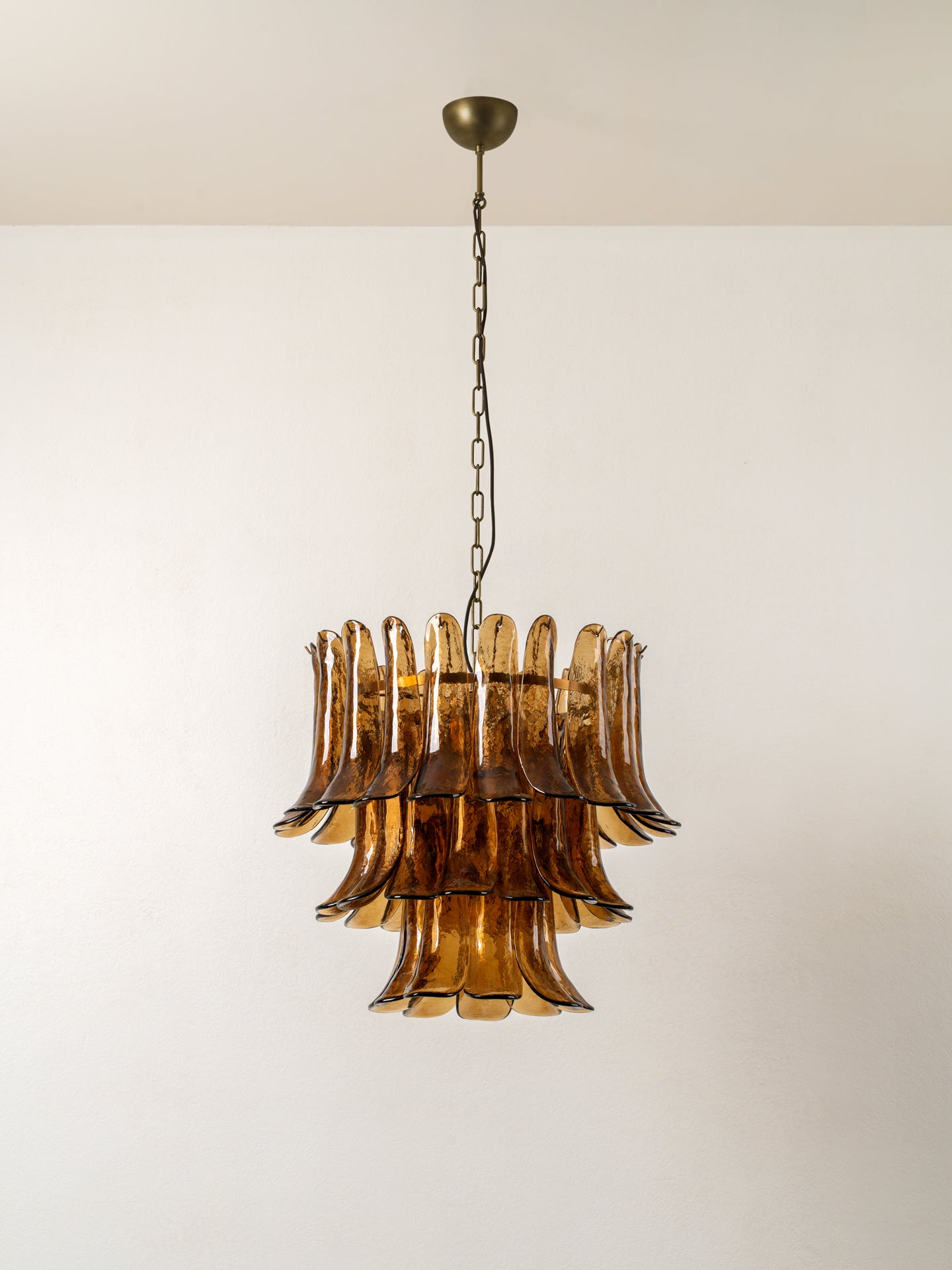 A mid-century modern tiered chandelier with amber brown smoked glass fluted shades, suspended from a brass ceiling canopy by a dark metal chain.