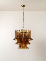 A mid-century modern tiered chandelier with amber brown smoked glass fluted shades, suspended from a brass ceiling canopy by a dark metal chain.