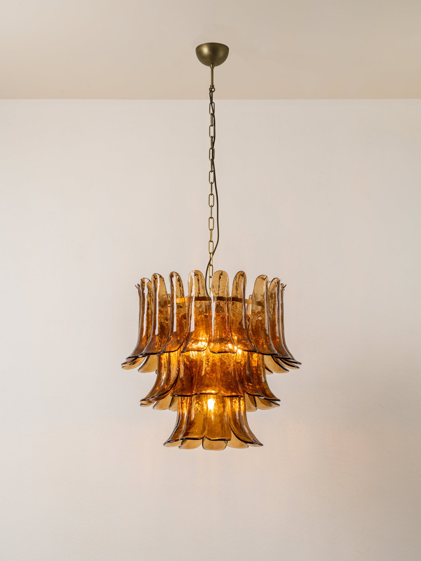 A vintage-style three-tiered amber glass chandelier pendant light hanging from a dark metal chain against a plain off-white wall.