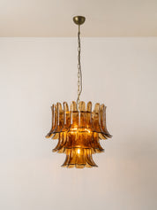 A vintage-style three-tiered amber glass chandelier pendant light hanging from a dark metal chain against a plain off-white wall.