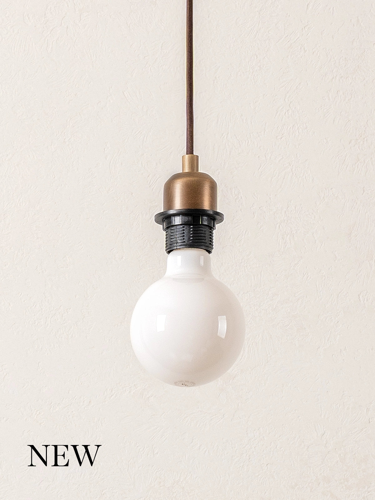 Aged brass pendant light with a white bulb on a plain background