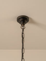 A close-up of a dark metal ceiling canopy and hanging chain fixture against a plain off-white wall.