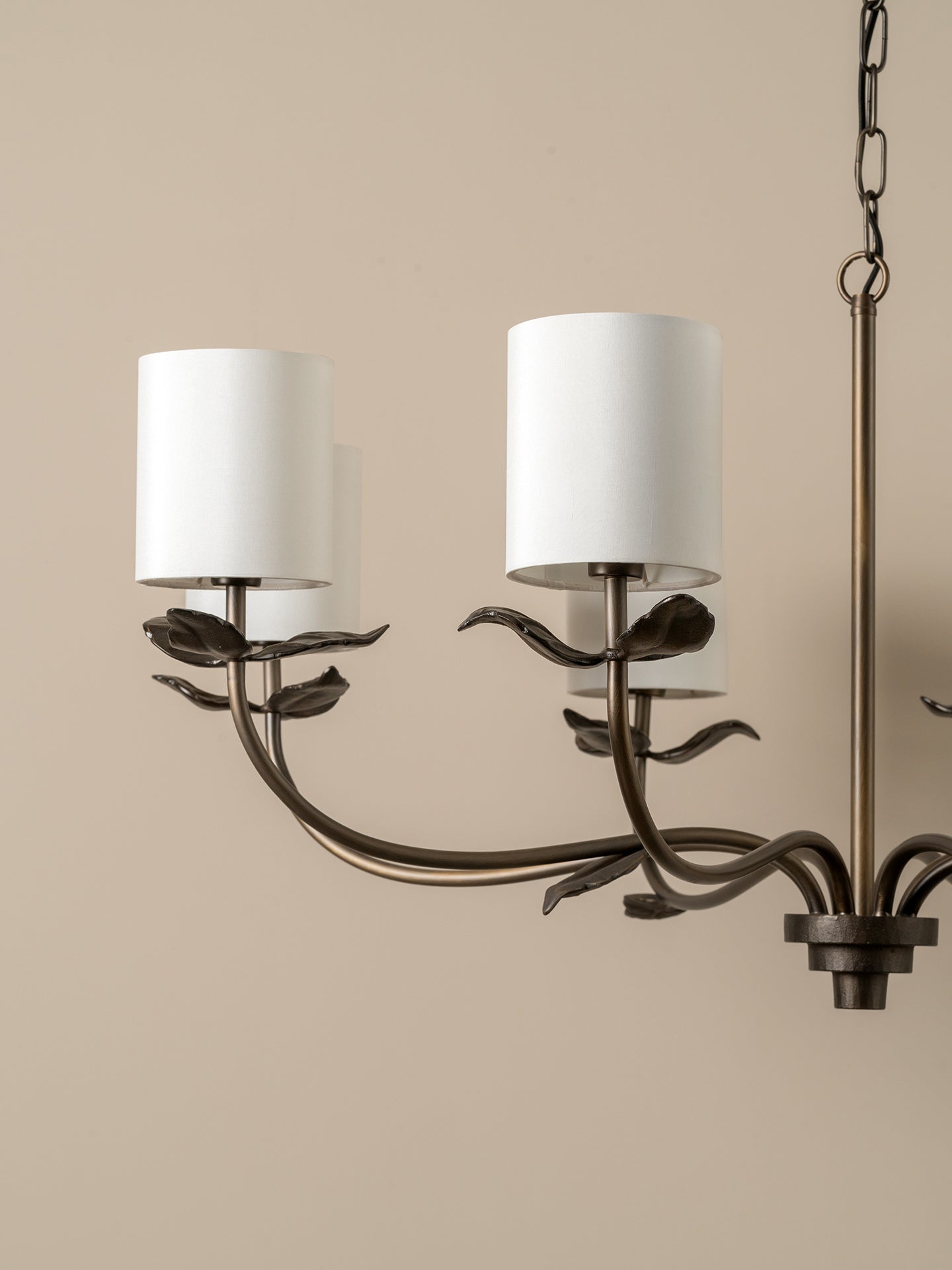 A close-up of a dark metal ceiling canopy and hanging chain fixture against a plain off-white wall.