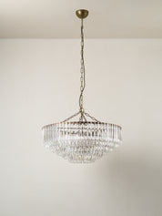 A tiered crystal chandelier with an antique bronze metal frame and chain, suspended from a ceiling against a plain off-white wall.