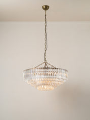 A tiered crystal chandelier with a bronze-finished metal frame and chain, suspended from a ceiling against a plain off-white wall.