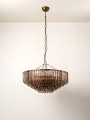 A round pendant chandelier with a bronze-finished metal frame and hanging glass shades, suspended from a chain against a plain off-white wall.