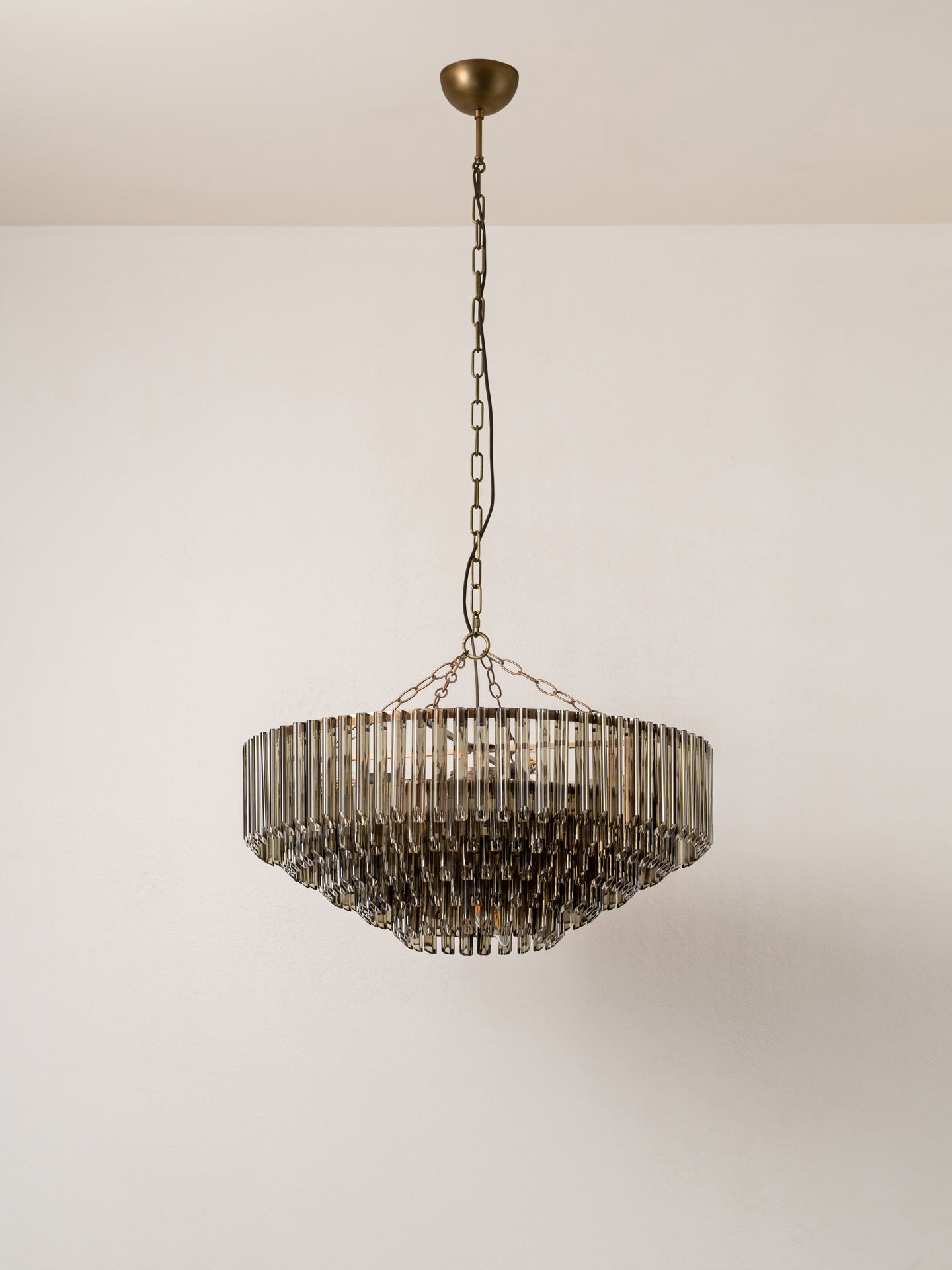 A modern tiered chandelier with a bronze-finished metal frame and hanging glass shades, suspended from a ceiling by a chain.