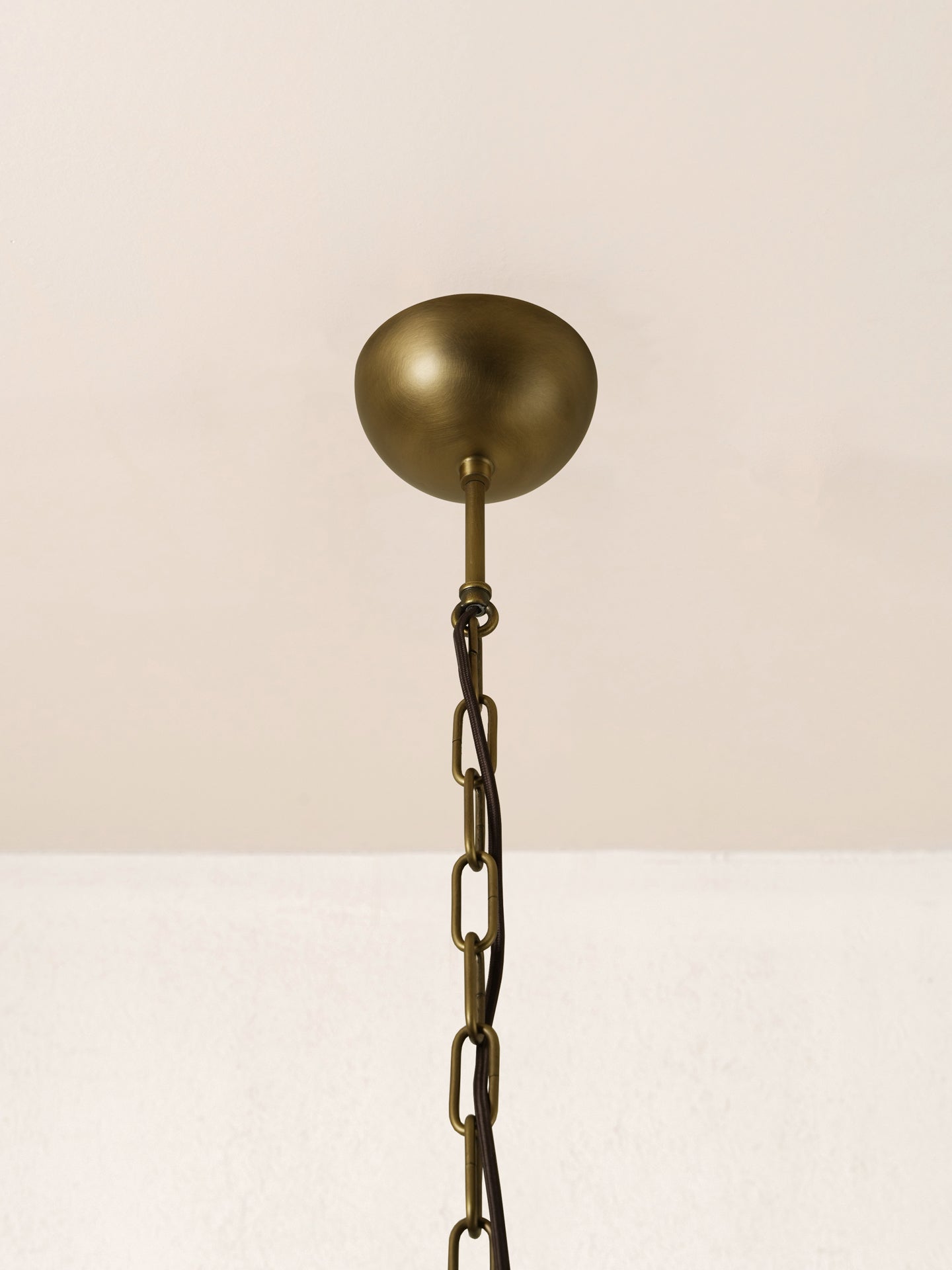 An antique brass ceiling canopy and chain hanger for a pendant light fixture, shown against a neutral off-white background.