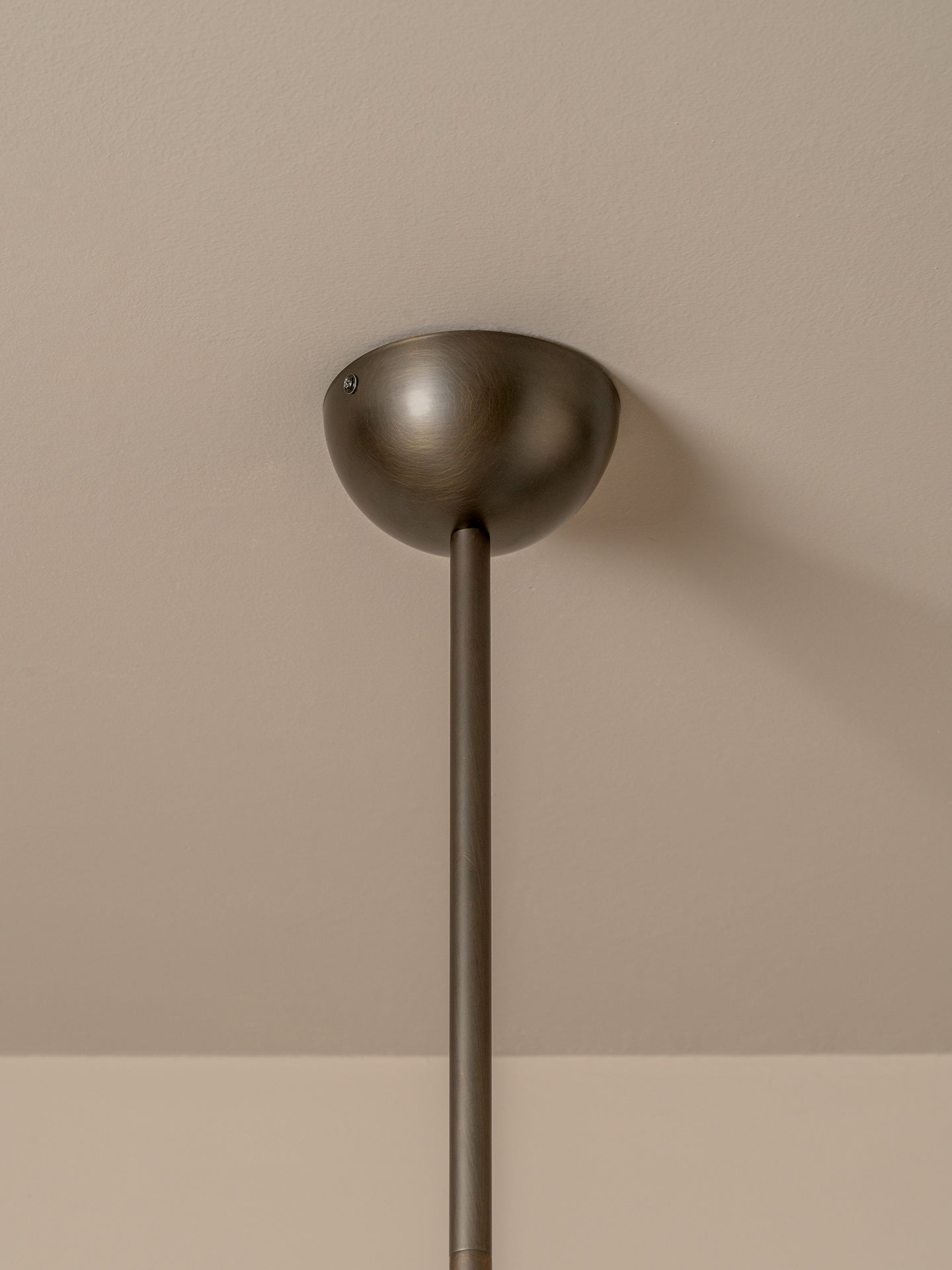 A close-up of a modern ceiling light fixture with a matte bronze dome shade and a matching vertical stem, mounted against a warm beige wall.