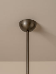 A close-up of a modern ceiling light fixture with a matte bronze dome shade and a matching vertical stem, mounted against a warm beige wall.