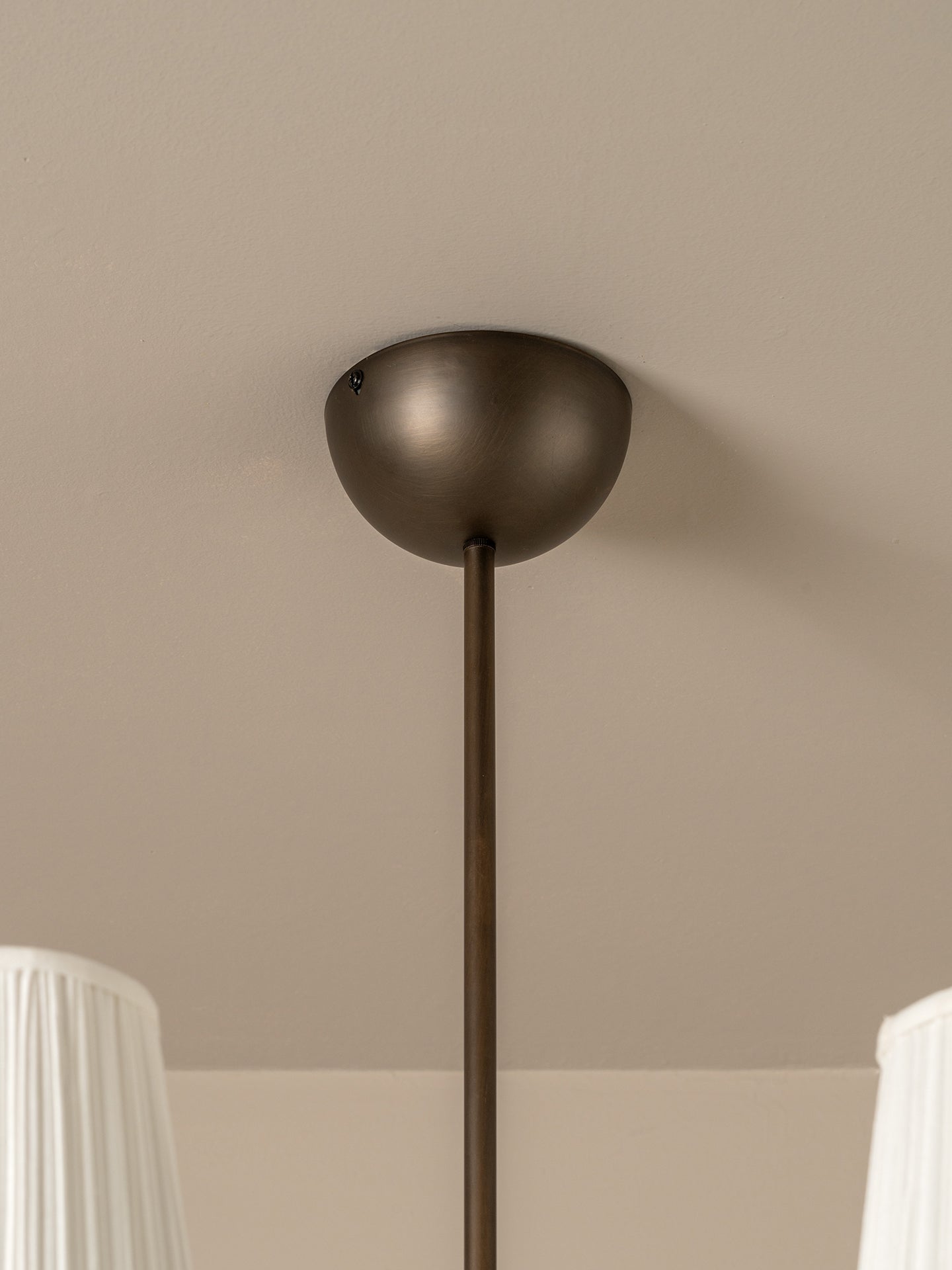 A close-up of a modern pendant light fixture with a matte dark bronze dome shade and a matching vertical rod, mounted on a beige ceiling.