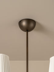 A close-up of a modern pendant light fixture with a matte dark bronze dome shade and a matching vertical rod, mounted on a beige ceiling.
