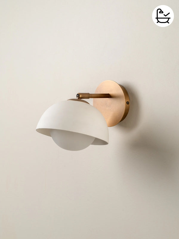 Wall-mounted light fixture with white shade and gold metal bracket on a beige wall.