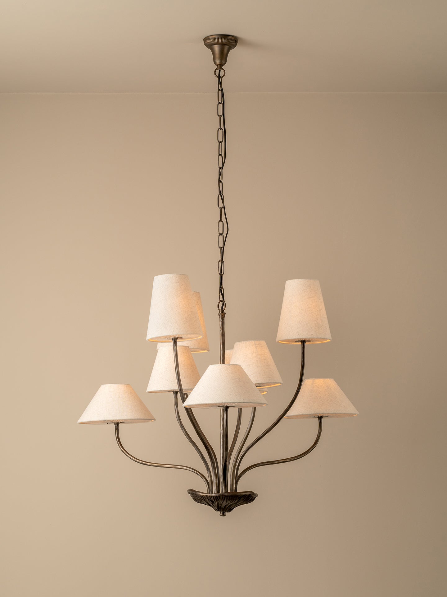 A multi-light chandelier with a dark bronze metal frame and seven tapered off-white fabric shades, hanging from a ceiling against a plain beige wall.