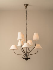 A multi-light chandelier with a dark bronze metal frame and seven tapered off-white fabric shades, hanging from a ceiling against a plain beige wall.