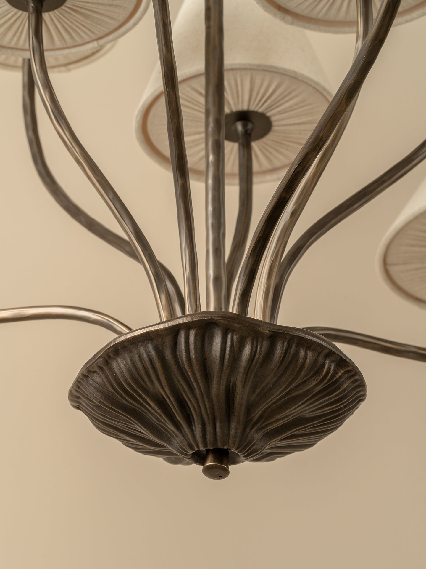 A close-up view of a multi-arm chandelier with a dark bronze central canopy and curved metal arms, shown against a warm beige ceiling.