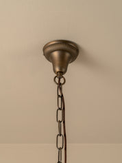 An antique bronze ceiling light fixture canopy with a decorative ribbed top and a hanging chain, shown mounted on a beige wall.