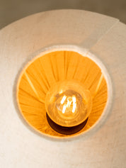 A close-up view of a warm glowing light bulb inside a textured beige fabric or paper lampshade.