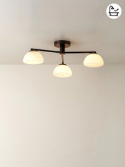 Ceiling light fixture with three round glass shades on a plain wall.