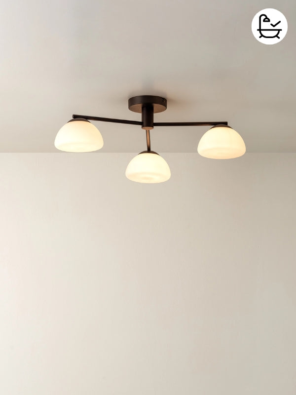 Ceiling light fixture with three round glass shades on a plain wall.