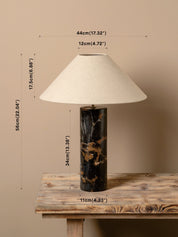 A table lamp with a cream fabric conical shade, a black marble base with gold veining, and overlaid dimension lines showing its height, width, and base width on a rustic wooden table against a beige wall.