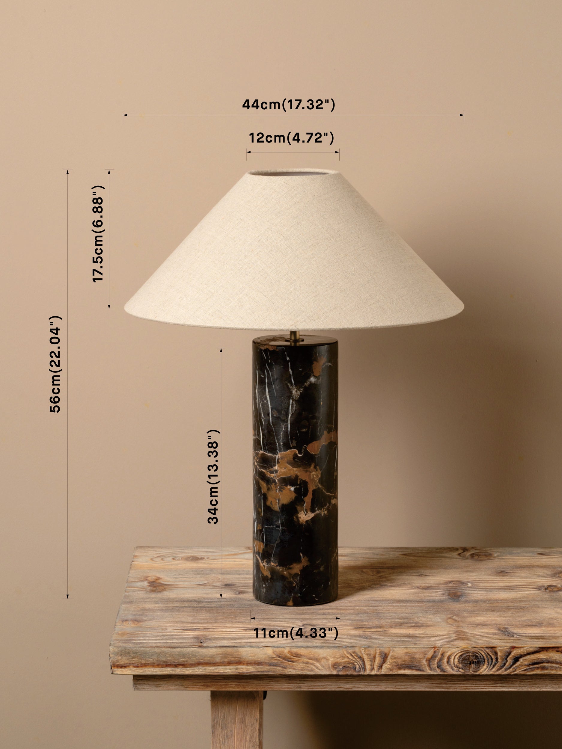 A table lamp with a cream fabric conical shade, a black marble base with gold veining, and overlaid dimension lines showing its height, width, and base width on a rustic wooden table against a beige wall.