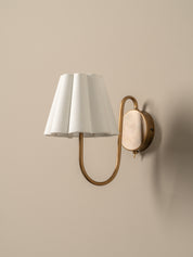 Wall-mounted lamp with white shade and gold arm on a beige wall